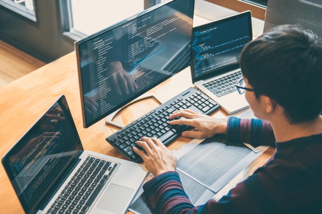 man typing on a keyboard at work with two laptops