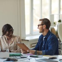 two colleagues discuss a report at their desks