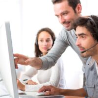a manager helping a colleague working on a help desk