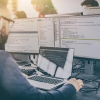 man with glasses working on a laptop with multiple screens